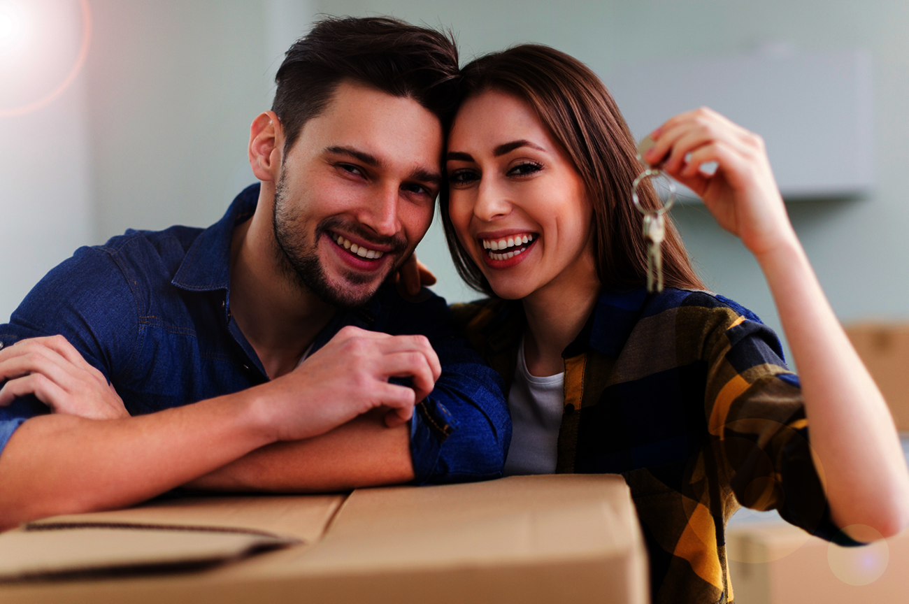 Lachende man en vrouw achter verhuisdozen en woningsleutels in de hand.